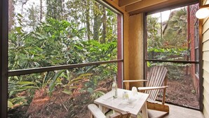 A wooden table with a bottle and glasses, a chair, and a view of dense greenery through large windows.