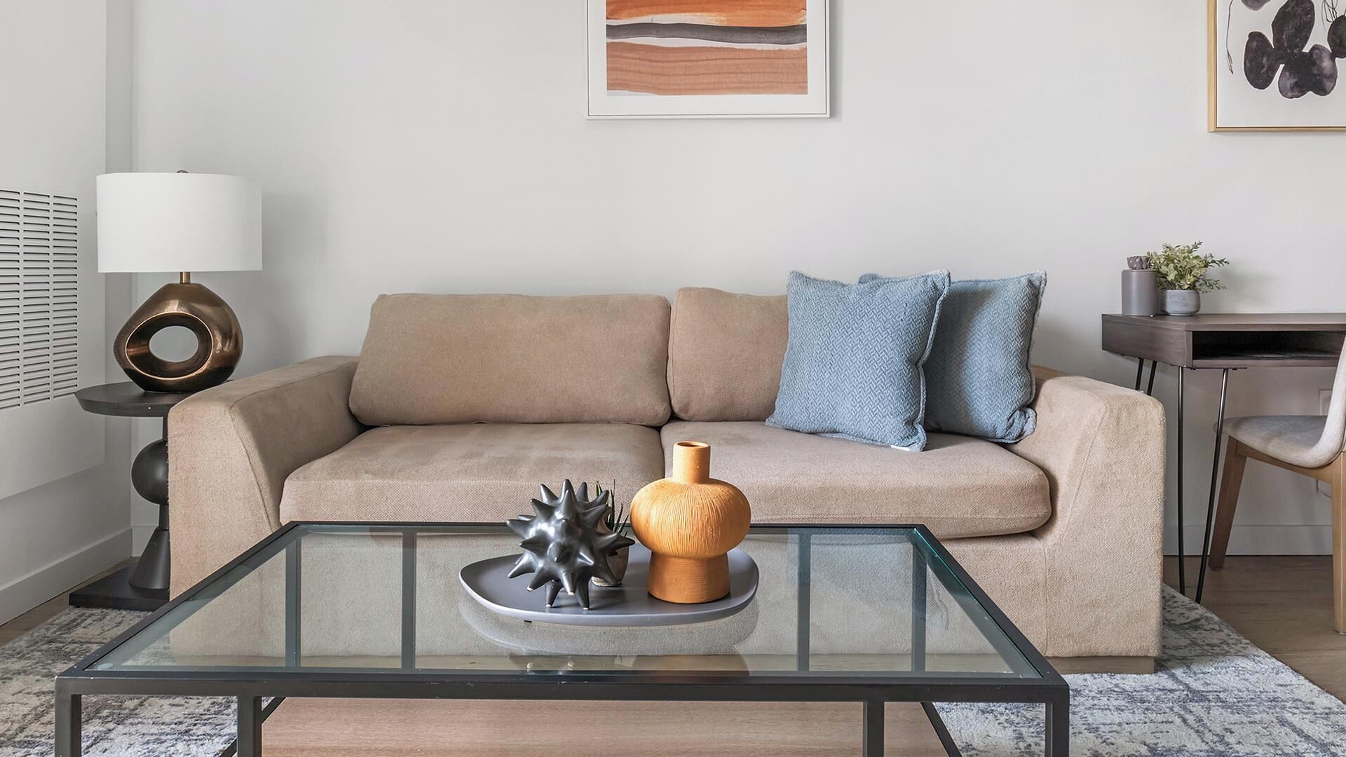 A modern living room with a glass coffee table, beige sofa, and decorative items.