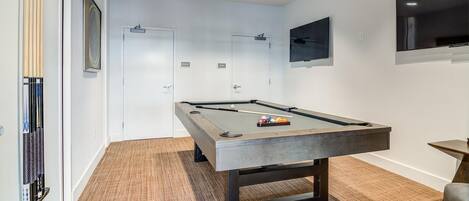 A pool table in a room with a carpeted floor, white walls, and a mounted television.