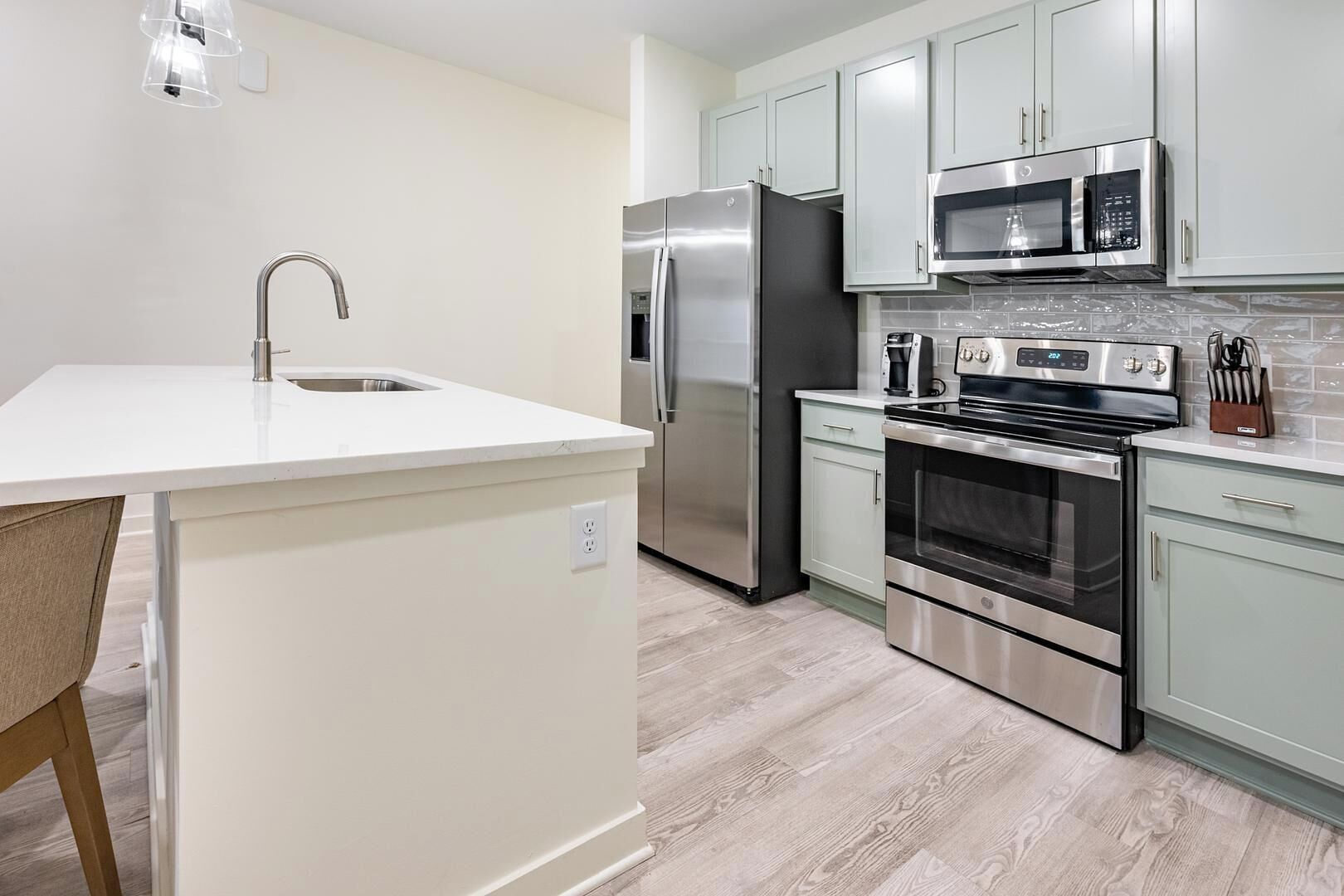 A modern kitchen with stainless steel appliances, a white countertop, and light green cabinets.