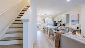 A modern kitchen with a central island, a dining area with a round table, and a staircase leading to another level. - Landing | Stunning 2BD, Gym, Clubhouse (Leland)