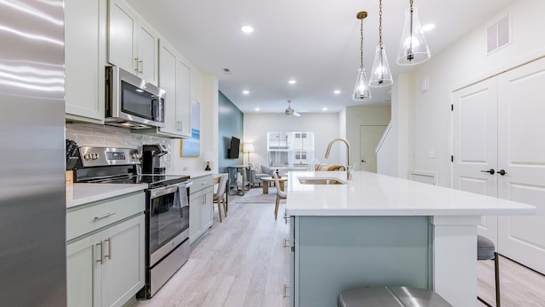 A modern kitchen with stainless steel appliances, a large island with a sink, and a seating area with a table and chairs. - Landing | Stunning 2BD, Gym, Clubhouse (Leland)