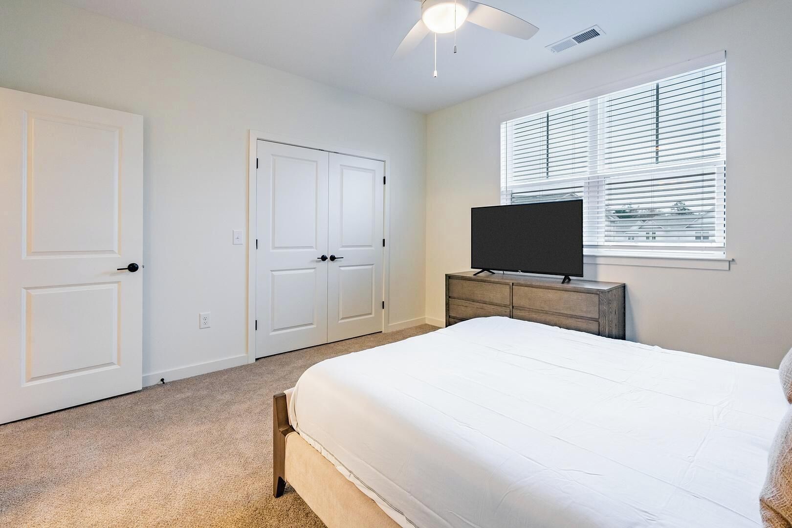 Een slaapkamer met een bed, een televisie op een dressoir en twee witte deuren.
