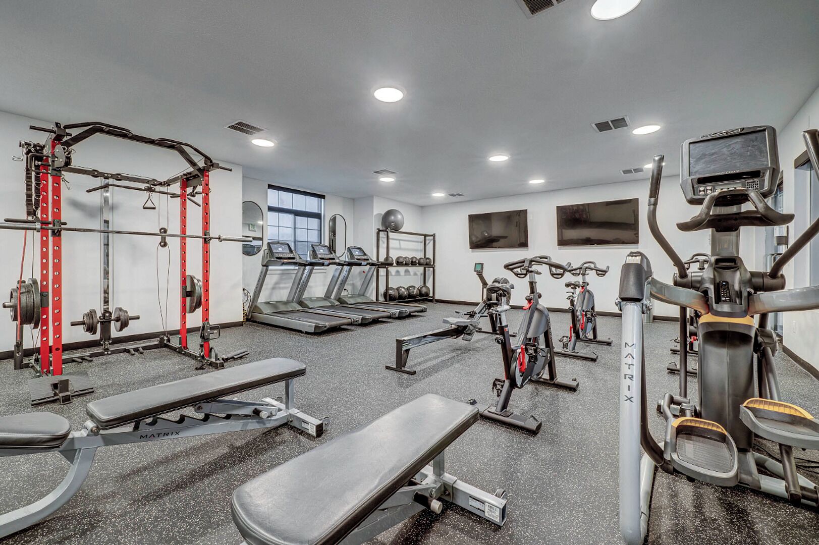Une salle de sport équipée de tapis de course, d’appareils de musculation et d’un banc.