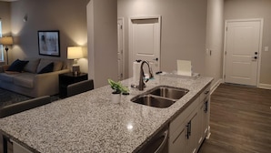 A modern kitchen with granite countertops, stainless steel appliances, and a two-basin sink. - Landing | Stunning 2BD, Gym, Pool (Newberry)