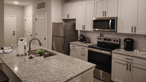 A modern kitchen with white cabinets, stainless steel appliances, granite countertops, and a built-in oven. - Landing | Stunning 2BD, Gym, Pool (Newberry)