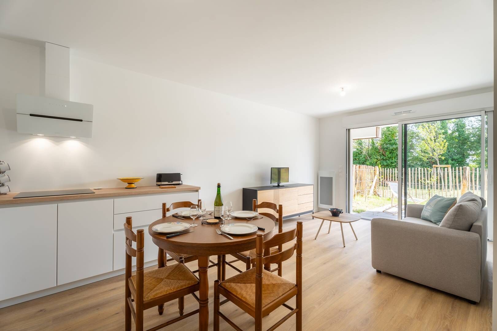 A modern kitchen with a dining area, a sofa, and a view of the outdoors.