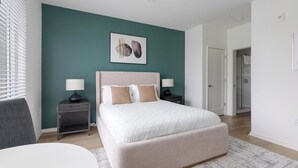 A bedroom with a bed, two bedside tables, a chair, and a painting on the wall. - Landing | Spectacular Studio, Rooftop Lounge, Gym (Durham)