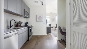 A modern kitchen with grey cabinets, a black faucet, and a microwave. There is a dining area with a table and chairs visible in the background.