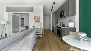 A modern hotel room with a bed, bedside table, lamp, and a view of the kitchen.