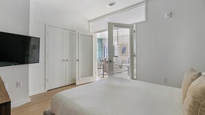 A bedroom with a bed, a TV mounted on the wall, and a door leading to a balcony.