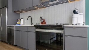 A modern kitchen with grey cabinets, a stainless steel refrigerator, a built-in oven, and a coffee machine.