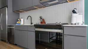 A modern kitchen with grey cabinets, a stainless steel refrigerator, a built-in oven, and a coffee machine.