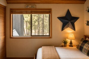 A bedroom with a bed, a star decoration, a lamp, and a window with blinds. - Black Butte Ranch House 034 (Black Butte Ranch)