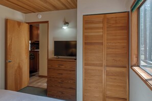 A bedroom with a wooden wardrobe, a television on a dresser, and a window with a view of the outdoors. - Black Butte Ranch House 034 (Black Butte Ranch)