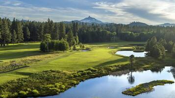 A golf course with a pond, trees, and a mountain in the background.