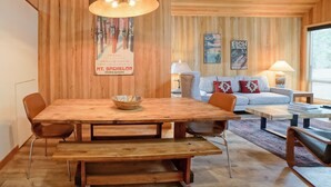A wooden dining table with a bowl, surrounded by chairs, in a room with wooden walls and a large window. - Black Butte Ranch House 036 (Black Butte Ranch)