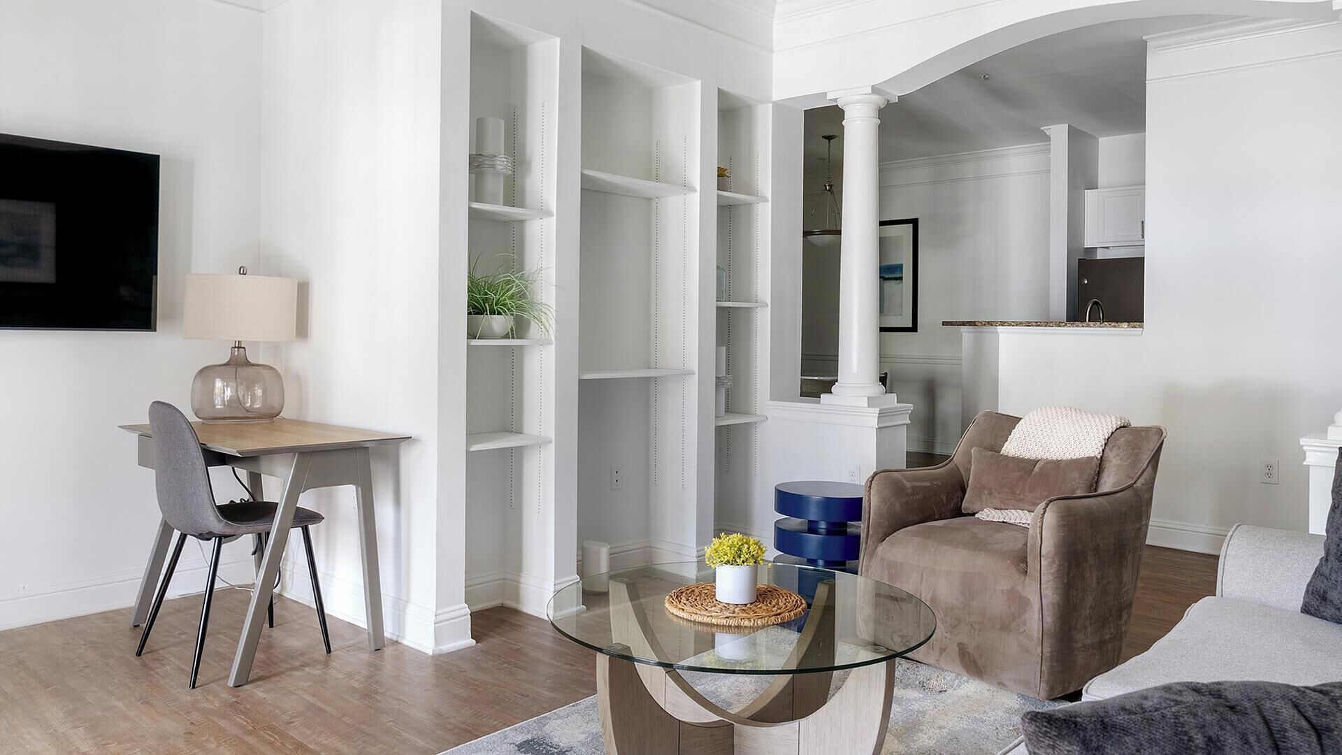 Un salon moderne avec une table basse en verre, un canapé marron et un coin repas comprenant une chaise et une lampe.