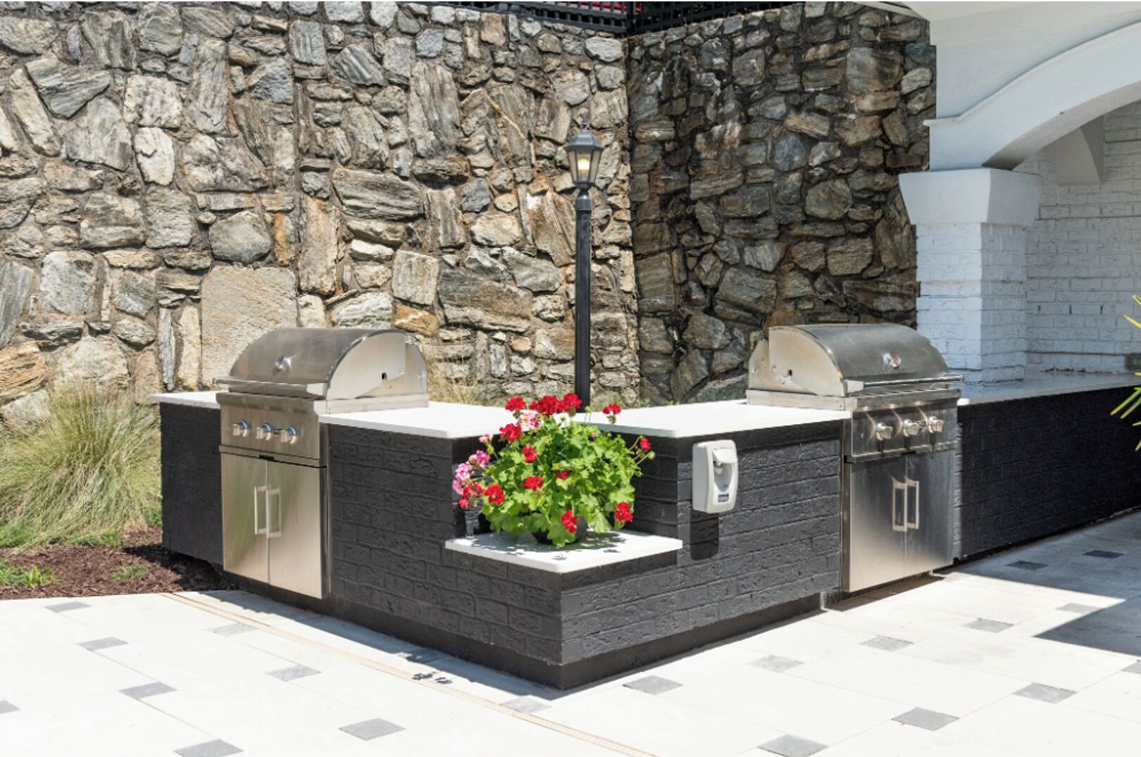 Cocina exterior con dos parrillas y jardinera integrada con flores.