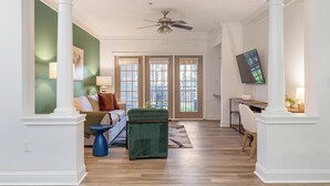A spacious living room with a green accent wall, a ceiling fan, and a large window with a view of the outdoors. - Landing | Incredible 2BD, Pool, Game Room (Buckhead)