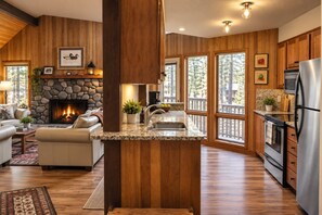 A modern kitchen with a stone fireplace, wooden cabinetry, and large windows. - Black Butte Ranch House 045 (Black Butte Ranch)