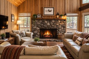 A cozy living room with a stone fireplace, leather sofas, and a flat-screen TV.
