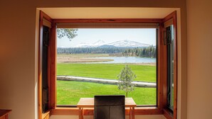 A room with a large window offering a view of a river, mountains, and a green field. - Black Butte Ranch Country House 065 (Black Butte Ranch)