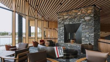 A modern lounge with stone walls, wooden ceiling, and large windows overlooking a body of water.