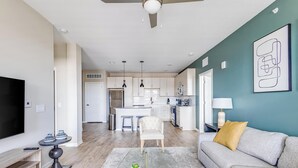 Un salon moderne avec un canapé gris, une table basse en verre agrémentée d’objets décoratifs, un téléviseur et un meuble TV en bois.
