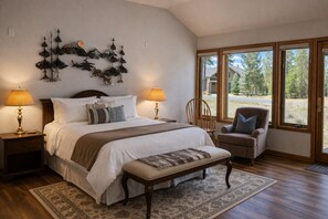 A bedroom with a large bed, two bedside lamps, a chair, a rug, and a wall-mounted decoration. - Black Butte Ranch East Meadow 017 (Black Butte Ranch)