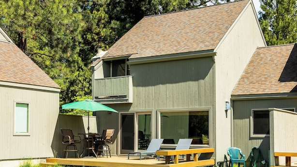 A two-story house with a deck, outdoor seating, and a sliding glass door.