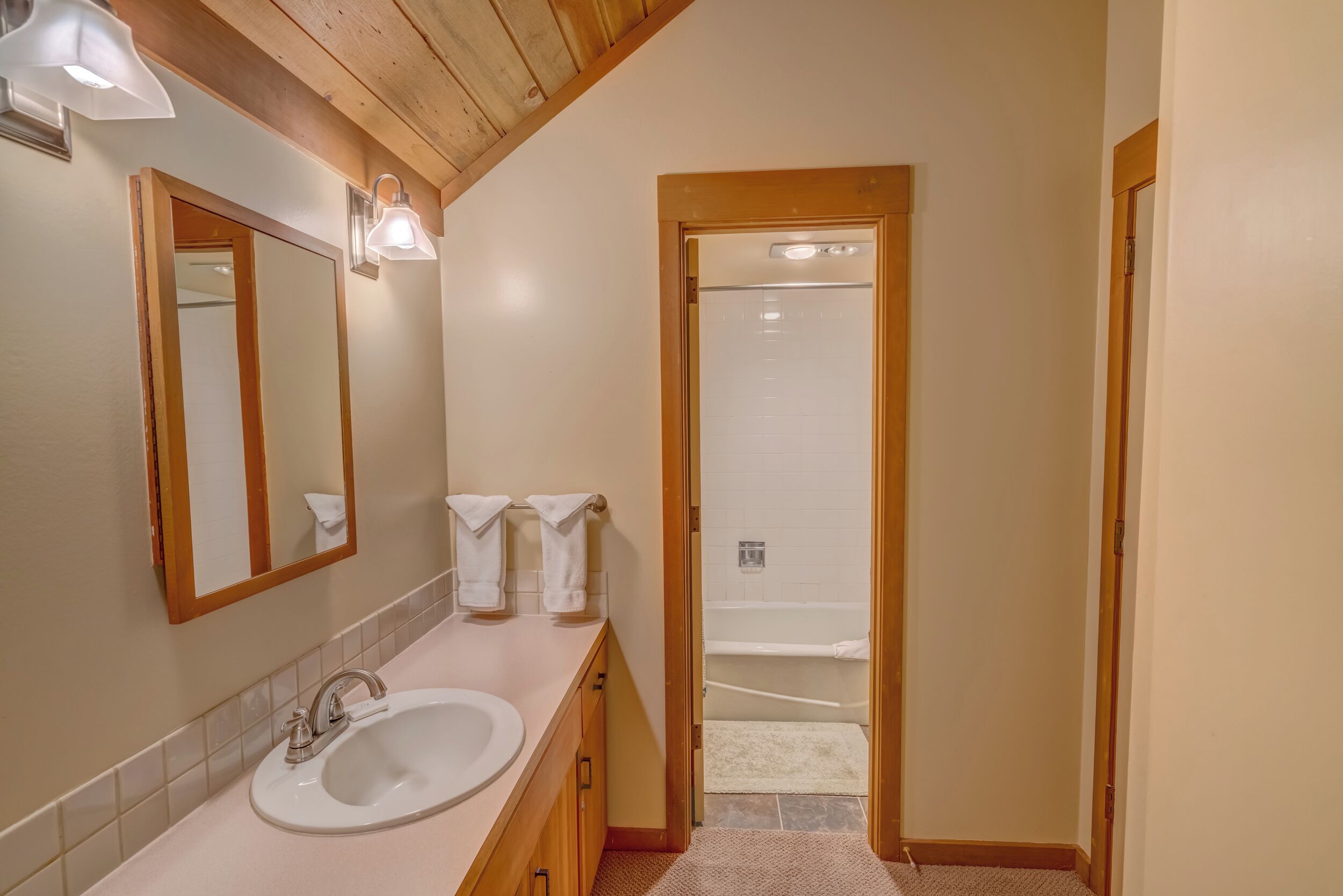 Une salle de bain avec un meuble-lavabo en bois, un évier, un miroir et deux appliques murales.