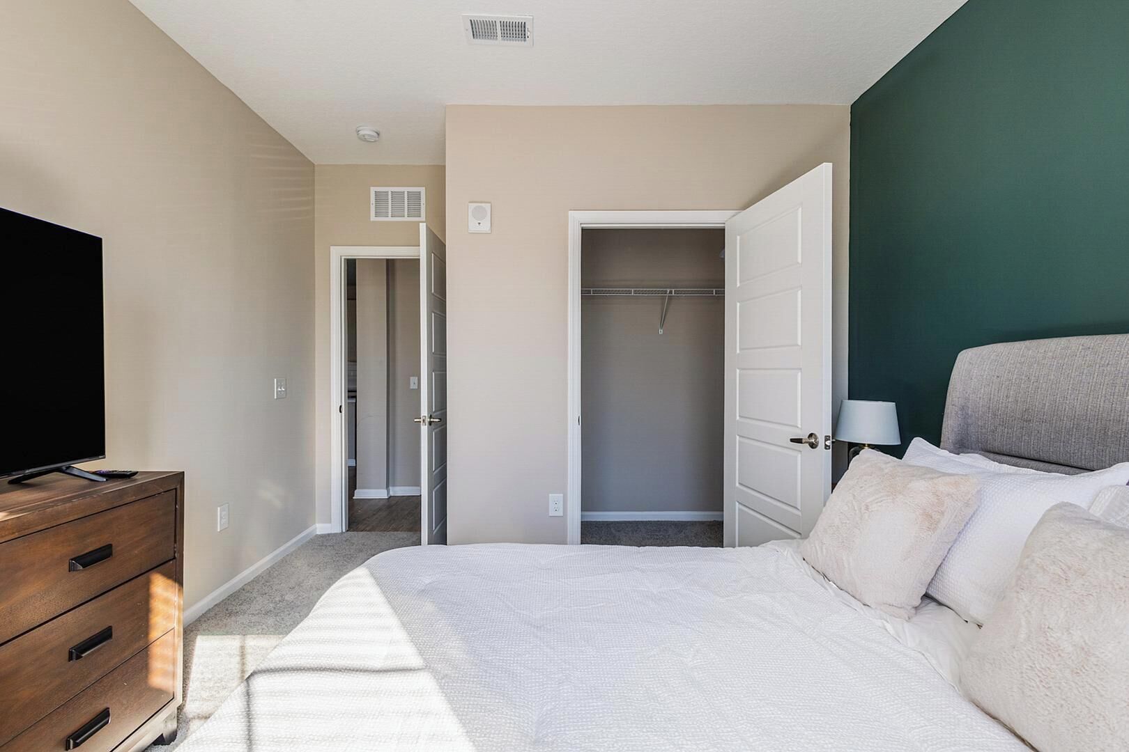 Une chambre d’hôtel avec un lit, un téléviseur posé sur une commode en bois, un dressing et un mur d’accent de couleur verte.