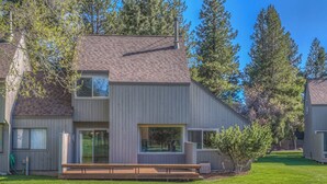 A modern two-story house with a large window, a deck, and a well-maintained lawn.