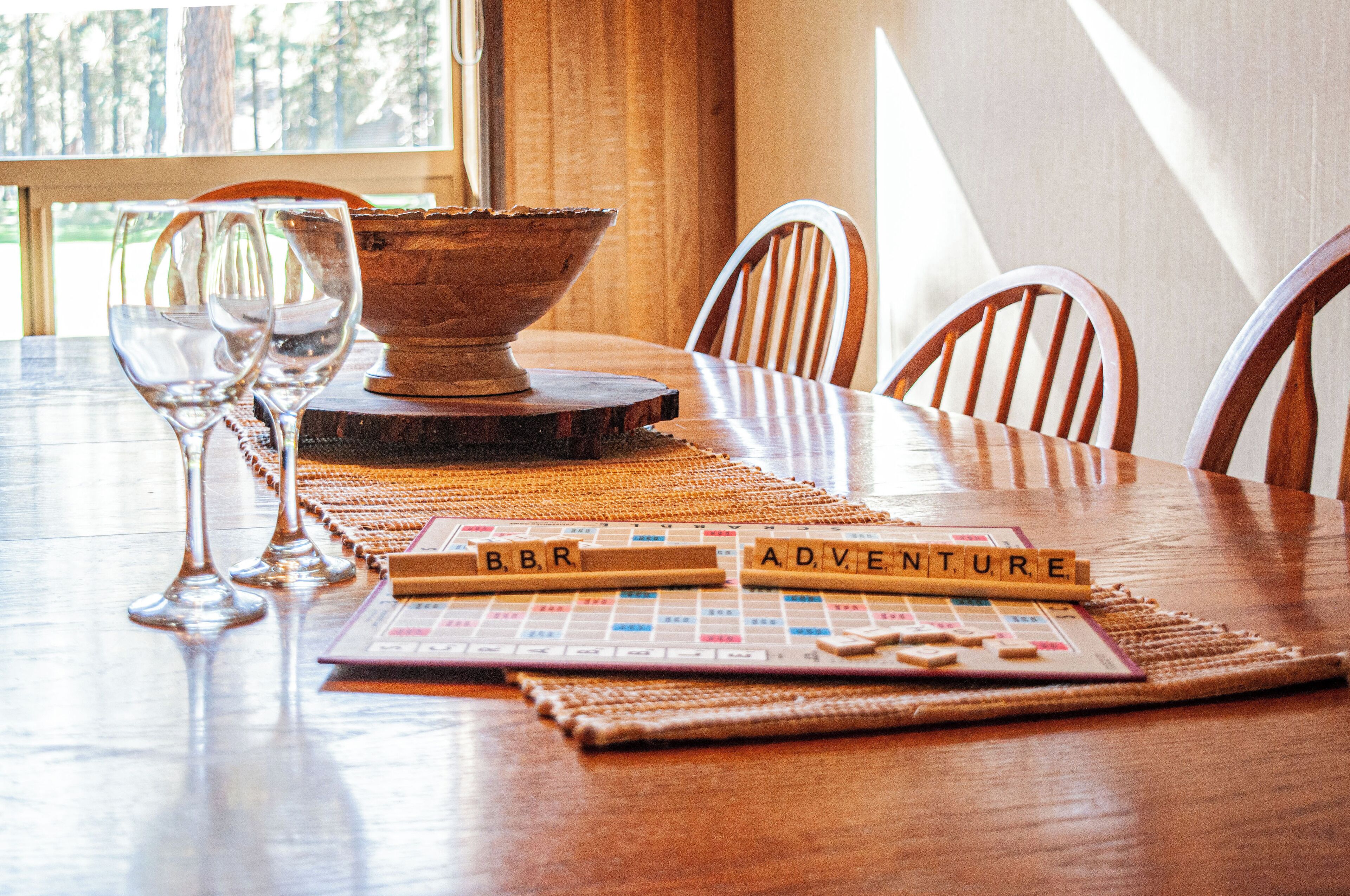Une table en bois, un jeu de Scrabble, deux verres à vin et un bol.