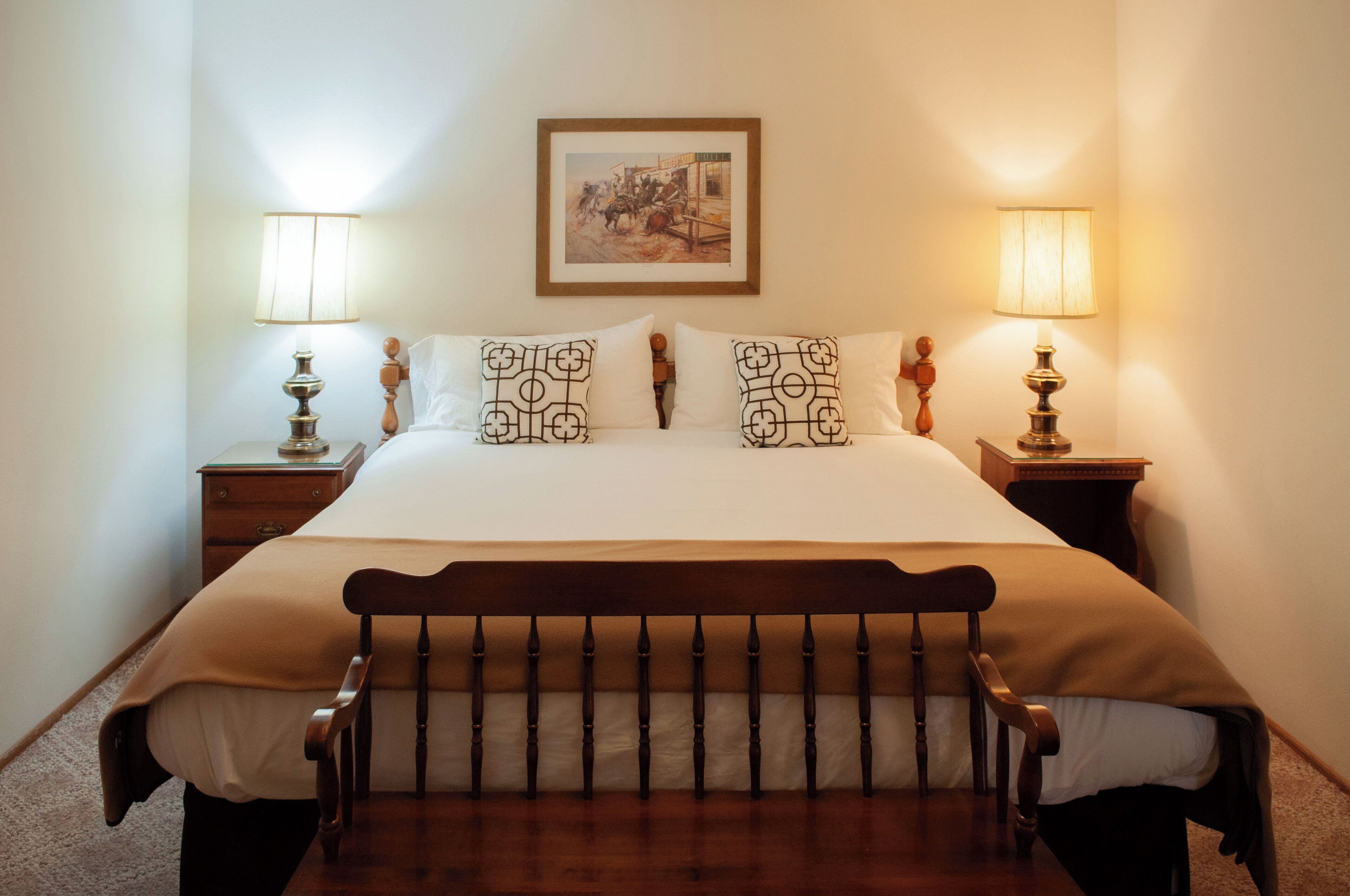 A neatly made bed with a wooden headboard, two bedside lamps, and a framed picture on the wall.