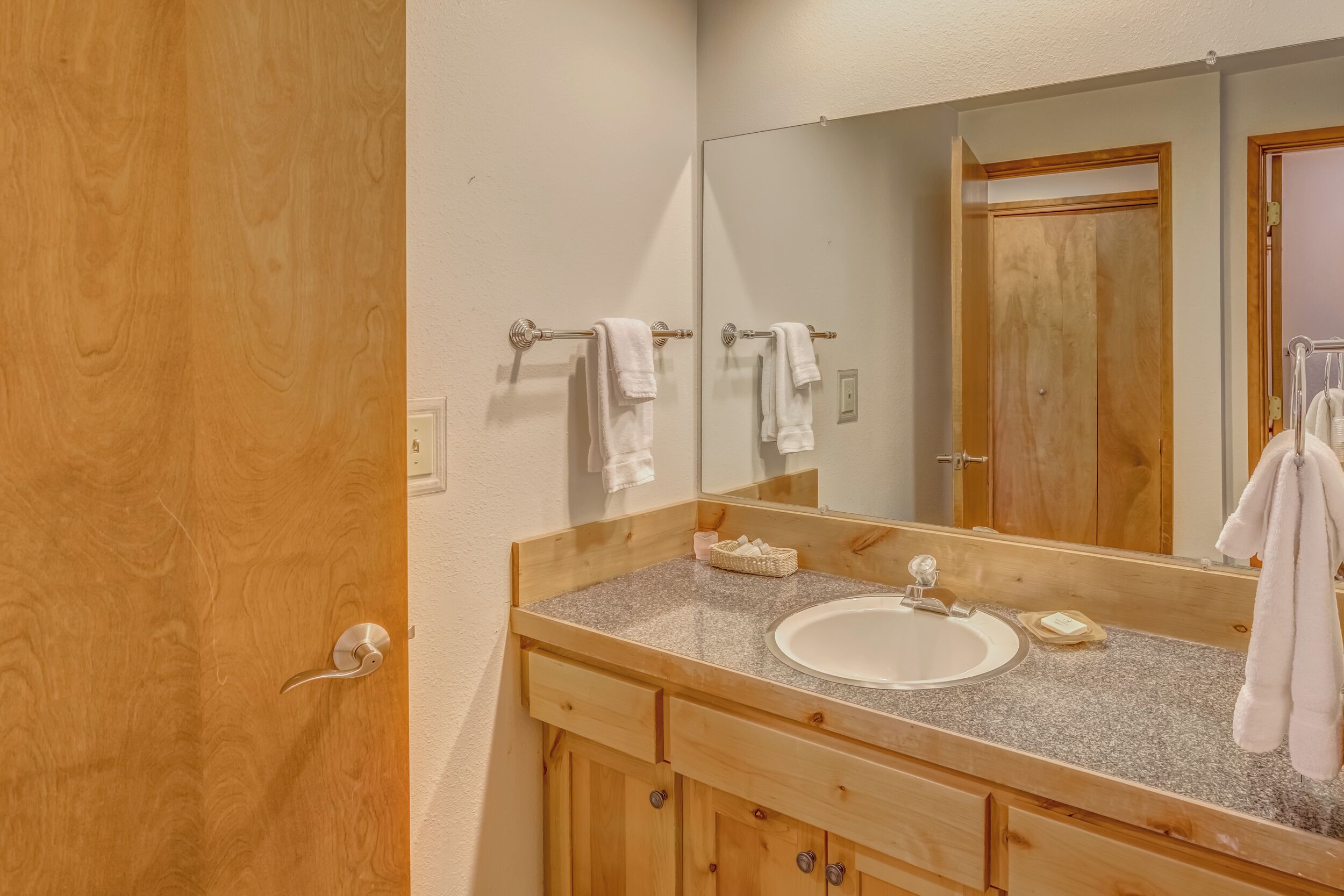 A bathroom with a wooden vanity, a white sink, and a large mirror.