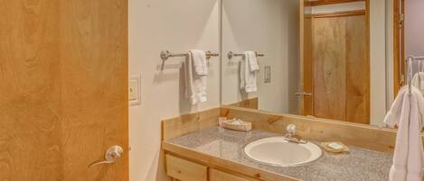 A bathroom with a wooden vanity, a white sink, and a large mirror.