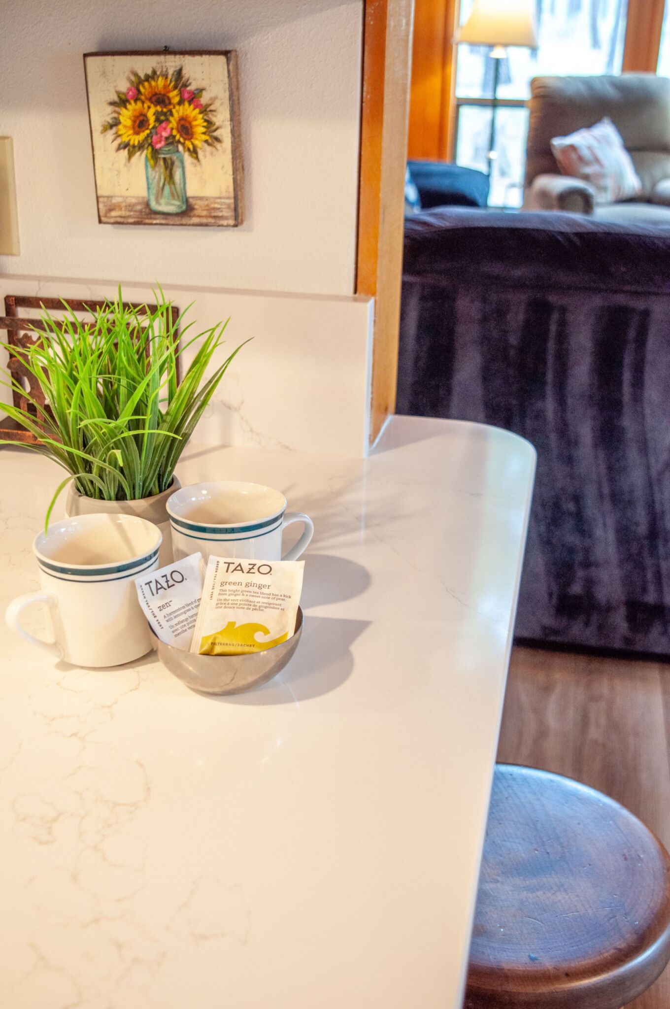 A kitchen counter with three white mugs, a packet of green ginger tea, and a potted plant.