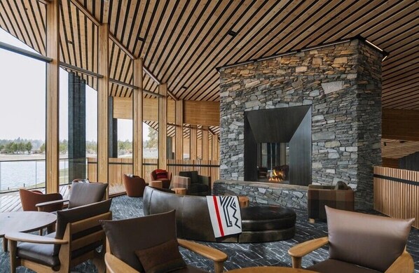 A modern lounge with stone walls, wooden ceiling, and large windows overlooking a body of water.