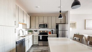 Une cuisine moderne avec des meubles en bois clair, des appareils en acier inoxydable, un îlot central et des luminaires suspendus.