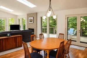 A modern living room with a wooden dining table, comfortable seating, a flat-screen TV, and a fireplace.