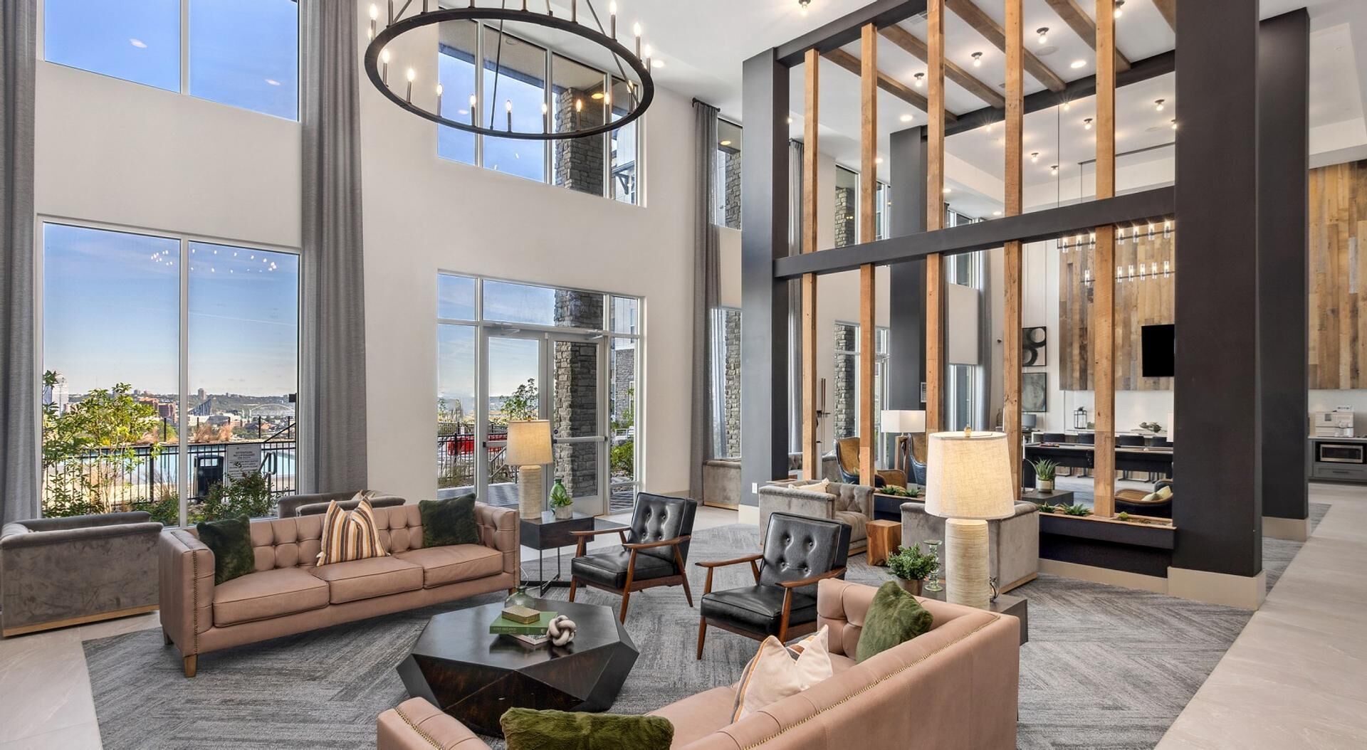 A spacious living area with a high ceiling, large windows, and a modern kitchen in the background.