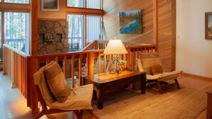 Un salon chaleureux avec une cheminée en pierre, une balustrade en bois et un tableau représentant une rivière.