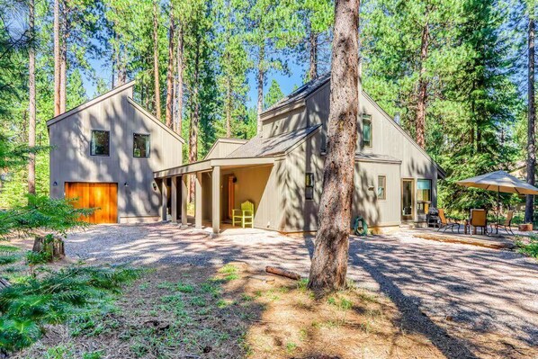 A two-story cabin with a covered porch, surrounded by tall pine trees. - Black Butte Ranch Golf Home 212 (Black Butte Ranch)