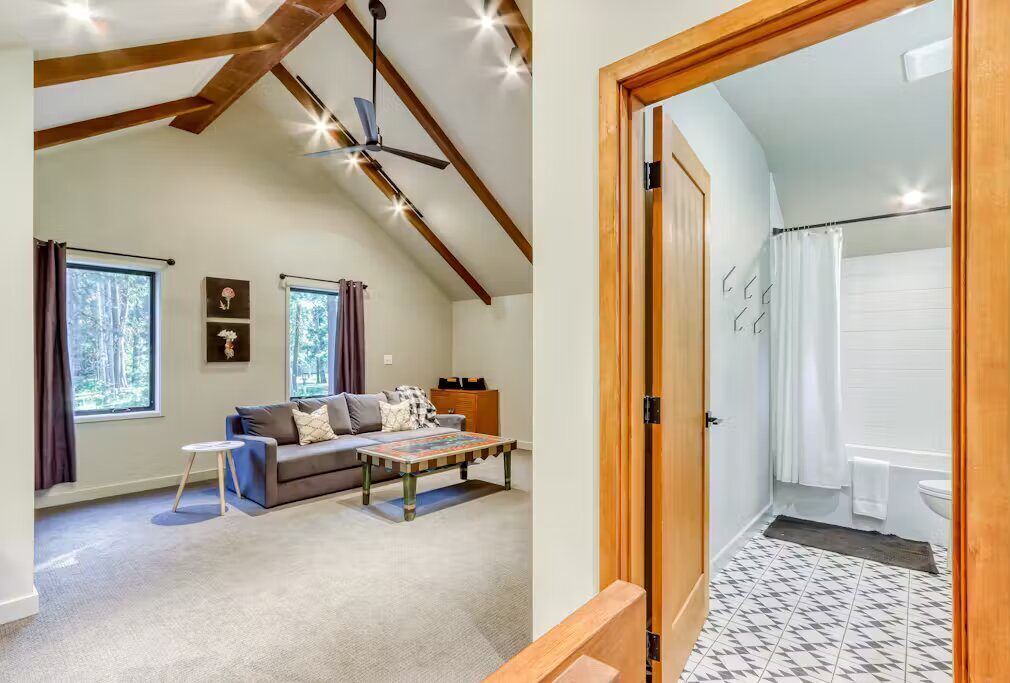 A spacious living room with a high ceiling, a sofa, a coffee table, and a view of the outdoors through large windows.