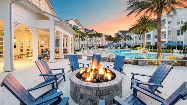 A poolside area with a fire pit surrounded by Adirondack chairs, a pool, and a building with a covered patio. - Landing | Incredible 1BD, Gym, Clubhouse (Nocatee)