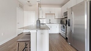 A modern kitchen with white cabinets, a stainless steel refrigerator, a microwave, and an oven. - Landing | Incredible 1BD, Gym, Clubhouse (Nocatee)