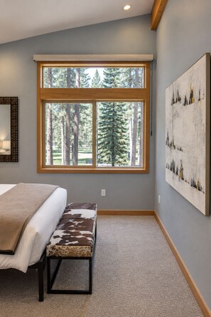 A bedroom with a large window, a bed, a bench, and a painting on the wall.