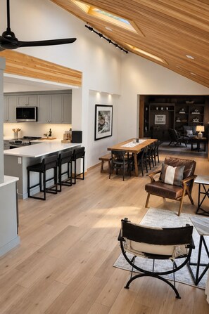 A spacious kitchen with a central island, a dining area with a long table, and a cozy seating area with a leather sofa.